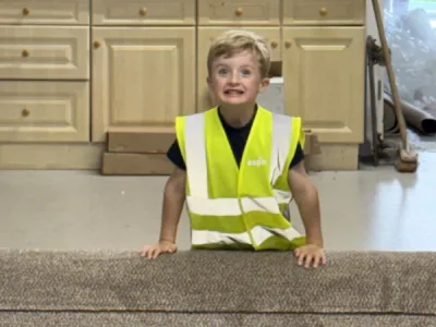 5 year old Ted in the cutting area standing behind a roll of carpet